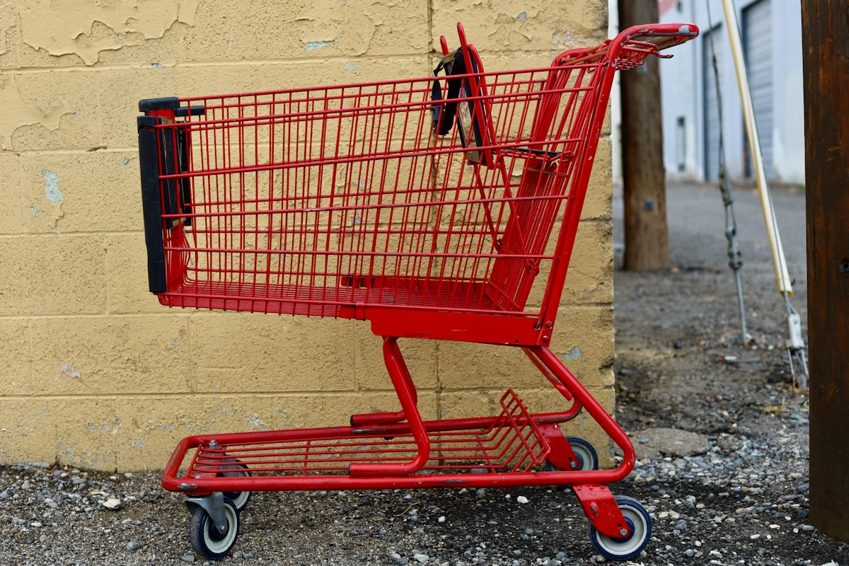 Carrello della spesa rosso lasciato su un pavimento di cemento grigio