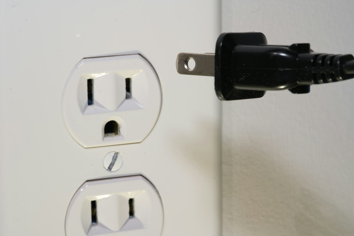 Spina nera davanti a una presa elettrica a muro